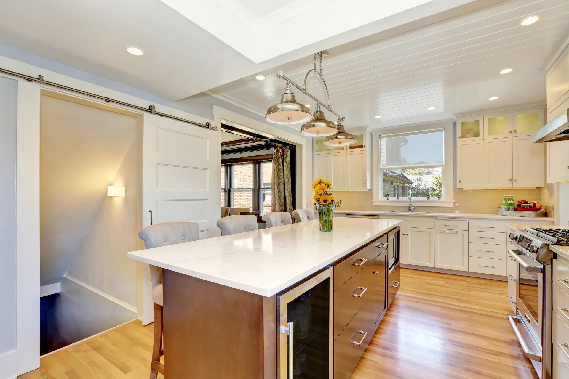 A photo of a kitchen with white cabinets on the far wall and an island with a white marble top and brown wood drawers in the center.