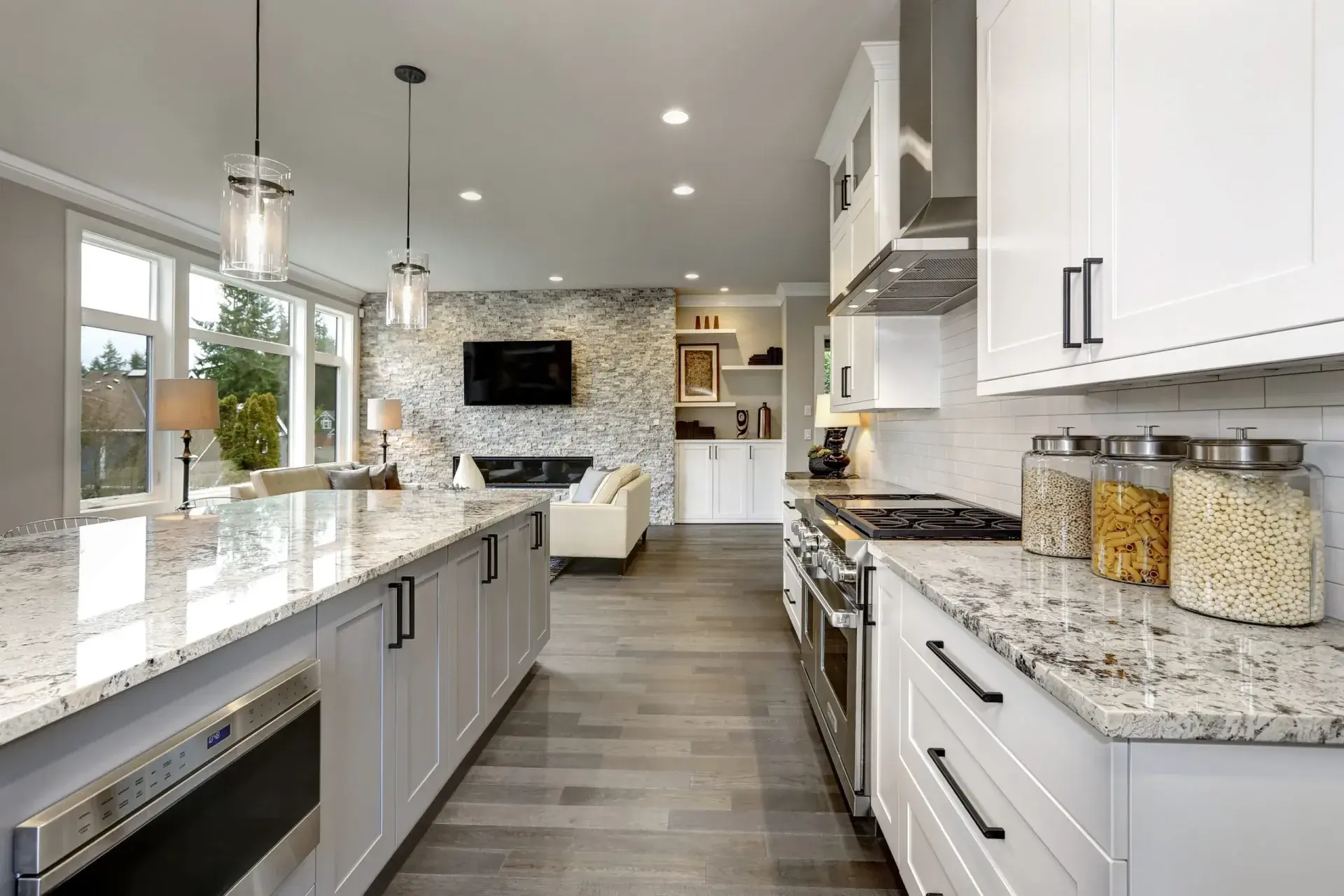 A kitchen with a large island on the left, white cabinets and oven on the right, and gray marbled countertop.