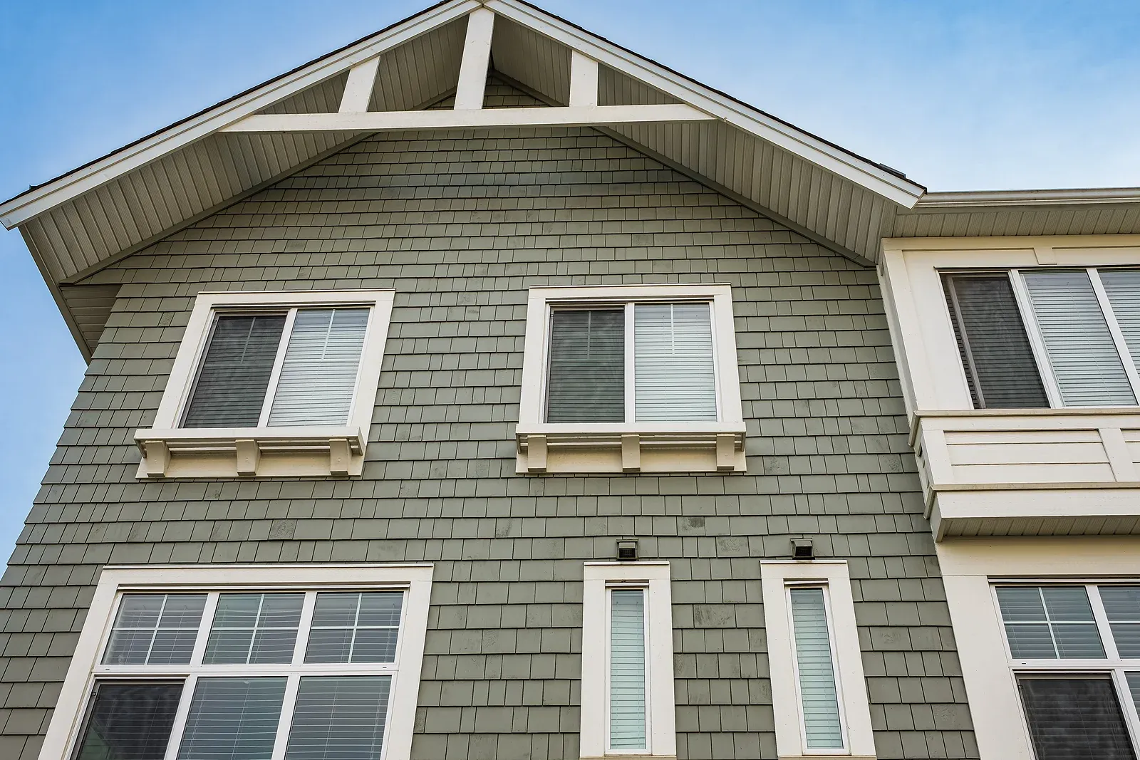 An upward angled photo of the facade of a house with green siding and several windows of varied sizes.