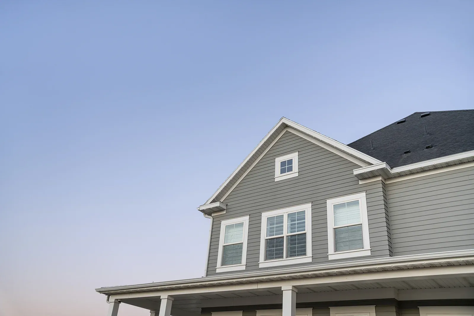 An upward-looking view of the second floor of a house with medium gray vinyl siding.